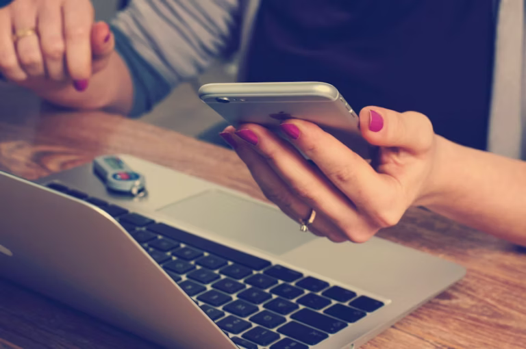 woman's hands holding phone with laptop open