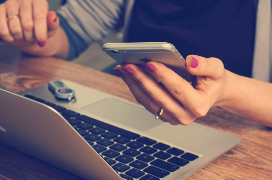 woman's hands holding phone with laptop open